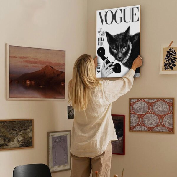 Woman hanging cat Vogue magazine parody artwork on eclectic gallery wall in bohemian home interior.