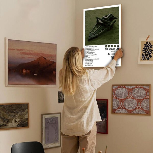 music-poster-gallery-wall-home-decor-styling.jpg Woman hanging Pierce The Veil album poster on eclectic gallery wall featuring various framed artworks in cozy home interior